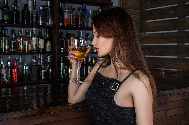 En kvinde står med en cocktail i hånden på en bar